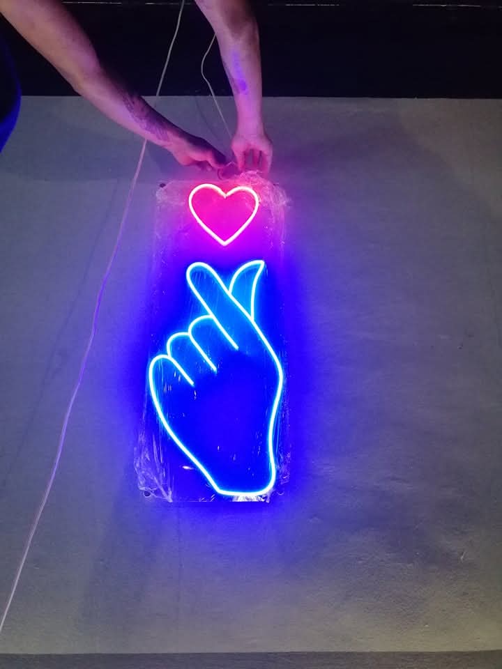Finger heart neon sign in blue and pink being installed