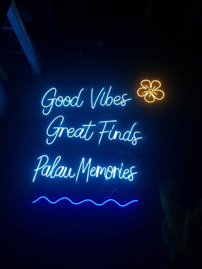 Blue script neon sign reading Good Vibes Great Finds with yellow flower