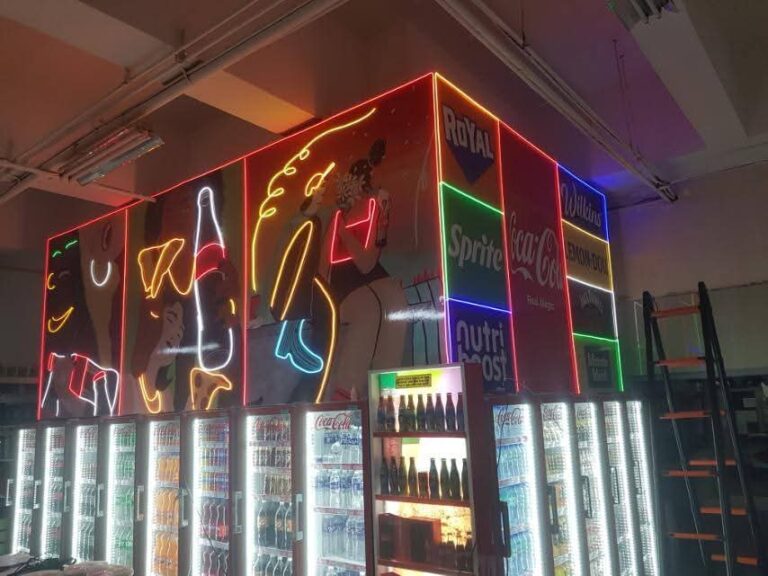 Retail store neon feature wall with outlined artwork above drinks coolers