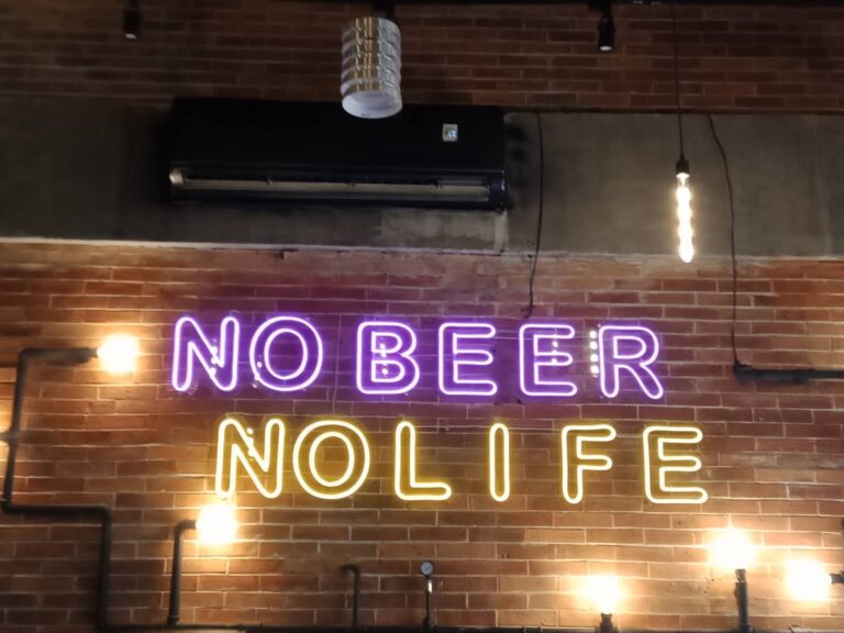 No Beer No Life neon sign in purple and yellow on a brick wall